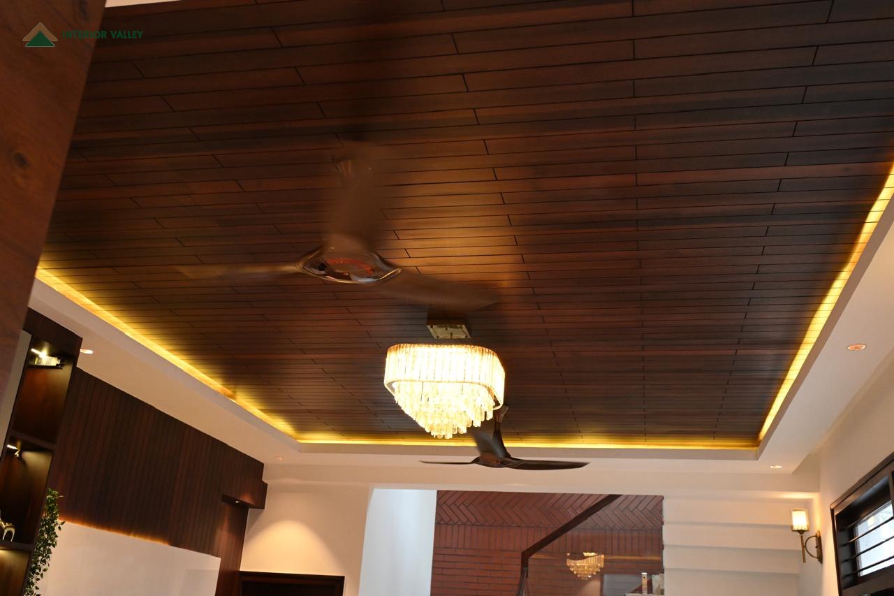 Wood-lined false ceiling with cove lighting and a chandelier