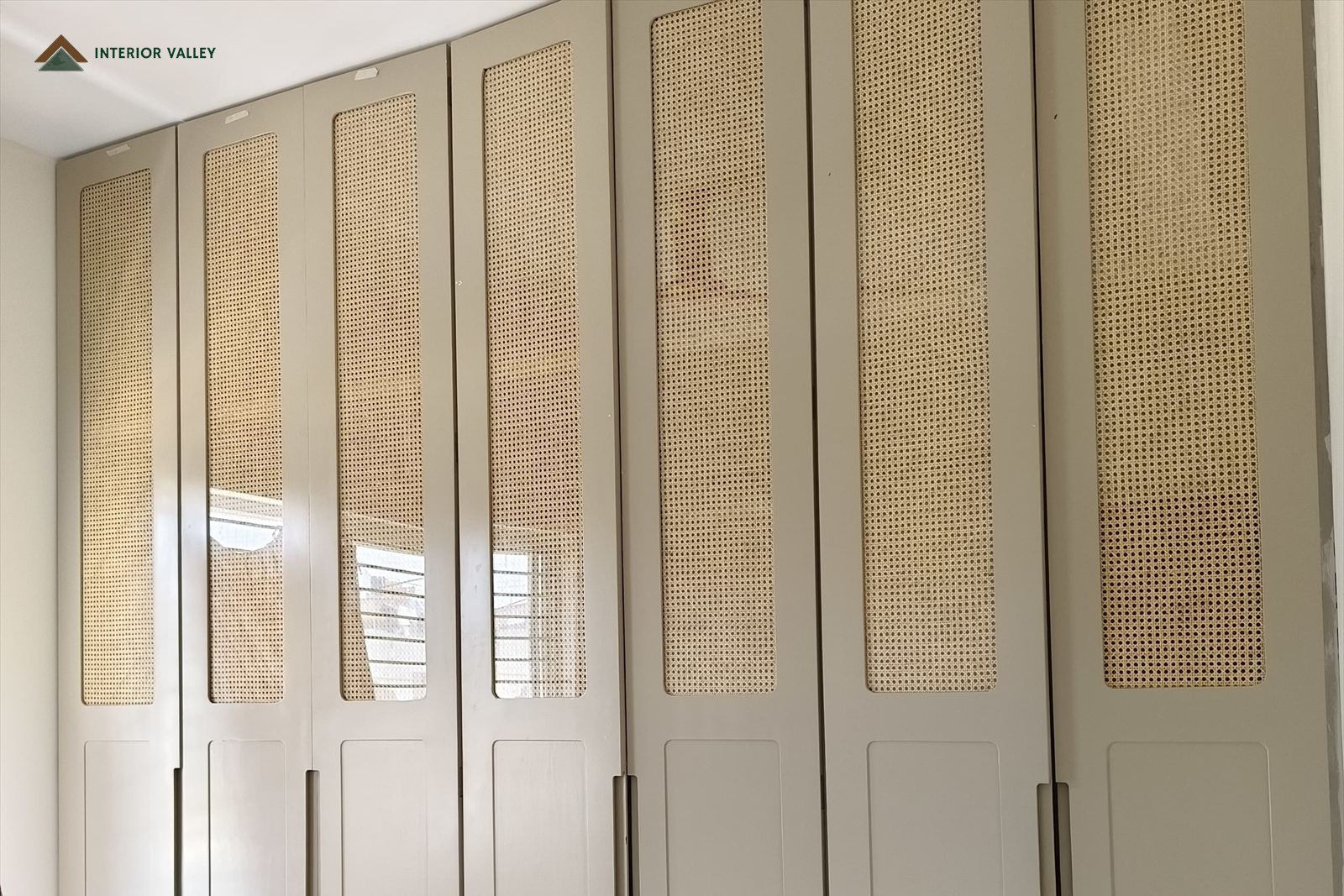Full-height wardrobe run in soft grey with cane panel inserts