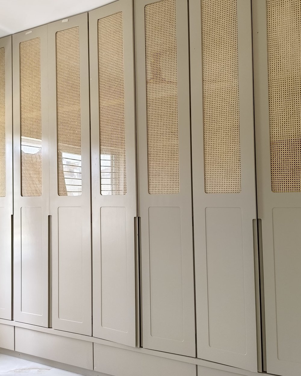 A full-height wardrobe run in soft grey with cane panel inserts